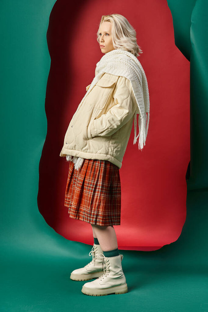 полная длина блондинка в стильном зимнем наряде позирует на красном с бирюзовым фоном - Фото, изображение
