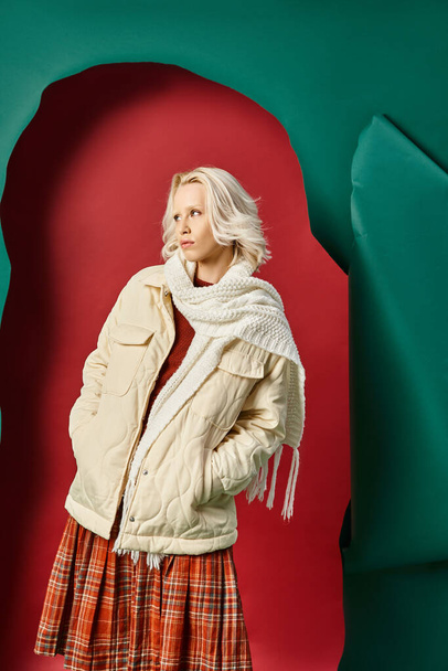жінка в стильній зимовій куртці, шарфі і плетеній спідниці дивиться на червоний з бірюзовим тлом - Фото, зображення