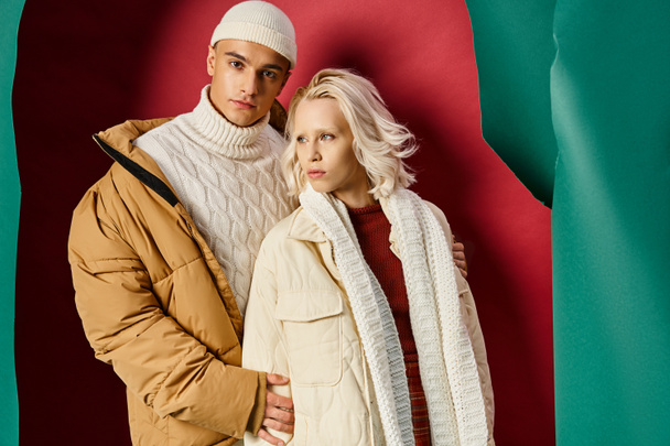 stylish man and woman in winter outerwear posing together on torn turquoise and red background - Photo, Image