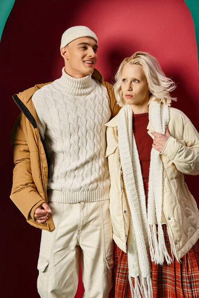 happy man and fashionable woman in winter outerwear posing on torn turquoise and red background - Photo, Image