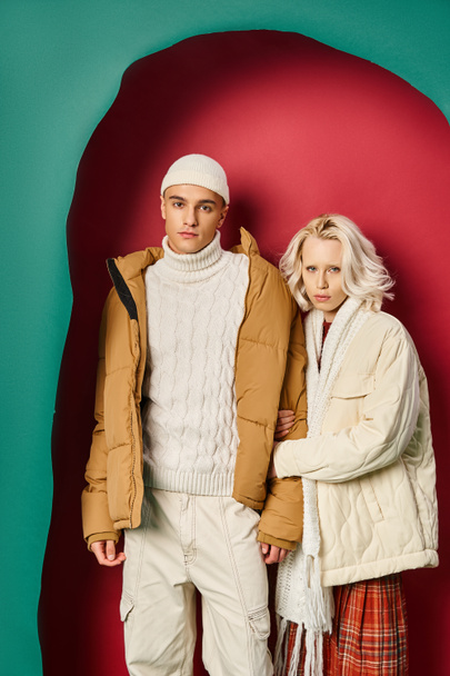 Sarışın, beyaz kışın dış giysili kadın yırtık turkuaz ve kırmızı arka planda bir adamın elini tutuyor. - Fotoğraf, Görsel