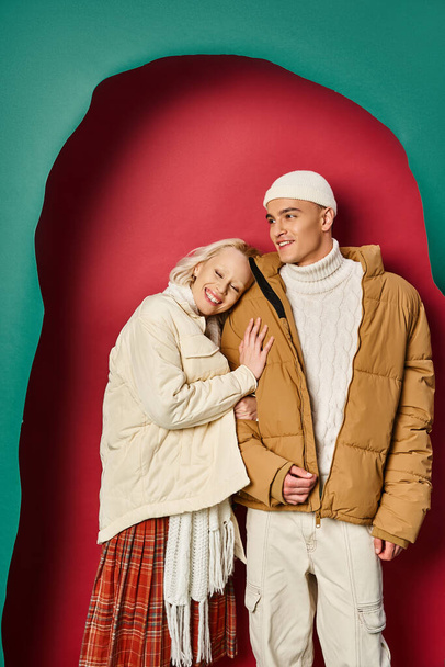 cheerful woman in winter jacket hugging stylish boyfriend near torn turquoise and red background - Photo, Image