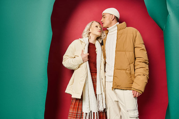 elegante jovem casal em elegante outerwear inverno abraçando perto rasgado turquesa e pano de fundo vermelho - Foto, Imagem