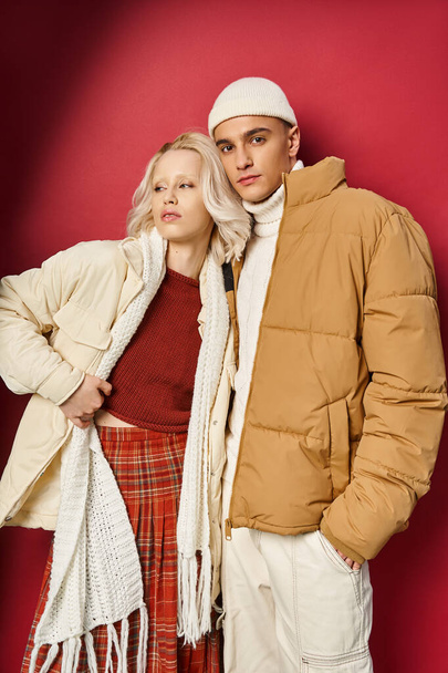stylish man and woman in warm winter outerwear posing together on red background, winter fashion - Valokuva, kuva