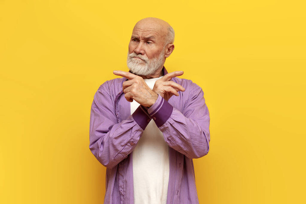 onzekere oude kale grootvader met grijze baard kiest en wijst op gele geïsoleerde achtergrond, dure bejaarde gepensioneerde wijst rond - Foto, afbeelding