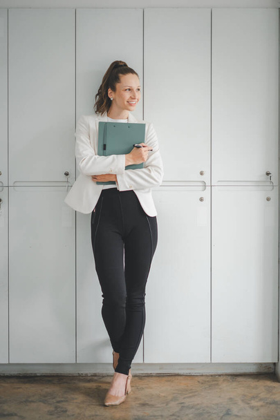 Επιτυχημένη επιχειρηματίας στέκεται στο δημιουργικό γραφείο και κοιτάζει έξω από τα παράθυρα. Γυναίκα επιχειρηματίας σε ένα χώρο συνεργασίας χαμογελώντας. - Φωτογραφία, εικόνα
