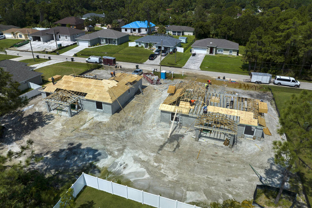 Vue aérienne des constructeurs travaillant sur la maison résidentielle inachevée avec structure à ossature de toit en bois en construction dans la zone de banlieue de Floride. - Photo, image