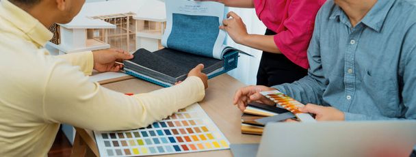 Εξειδικευμένη εσωτερική ομάδα σχεδιασμού προσεκτικά την επιλογή των υλικών κουρτίνας, ενώ ο συνάδελφος επιλέγοντας το χρώμα της κουρτίνας με το μοντέλο σπίτι τοποθετείται στο τραπέζι συνάντησης. Δημιουργική ιδέα σχεδιασμού. Ποικιλία. - Φωτογραφία, εικόνα
