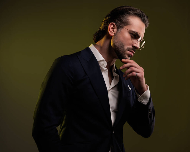 retrato de thoughtufl elegante hombre de negocios mirando a un lado, tocando la barbilla y pensando en frente de fondo amarillo - Foto, imagen