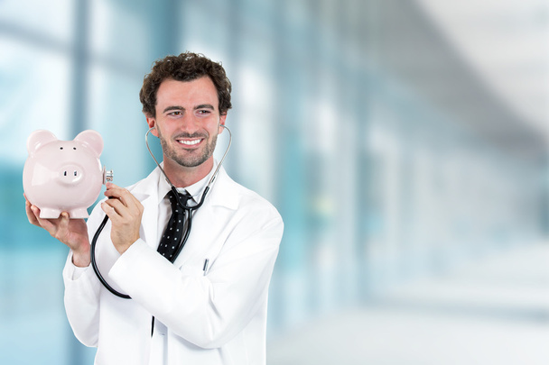 miling doctor holding listening to piggy bank with stethoscope - Foto, immagini