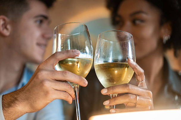 Kameralne zbliżenie młodego mężczyzny i kobiety wznoszących toast szklanką białego wina. Ich skoncentrowane wyrażenia i brzęk okularów symbolizują celebrację, więź i wspólne szczęście. - Zdjęcie, obraz