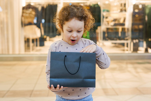 衣料品店のショッピングバッグを探している驚きと幸せな子供の少女 - 写真・画像