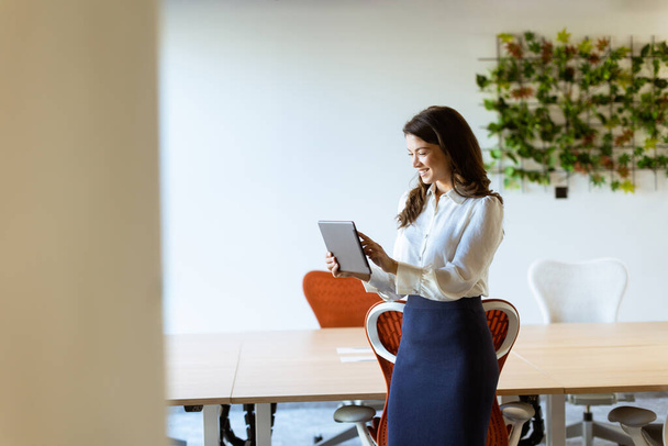 Jovem mulher de negócios com tablet digital em pé no escritório moderno - Foto, Imagem