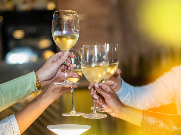Un primer plano de amigos levantando sus copas en un brindis, celebrando con vino blanco frío. El tono dorado del ambiente enfatiza la calidez de la reunión. - Foto, imagen