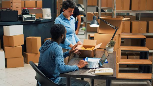 Team of startup partners doing quality control on products from storage room, checking cardboard packages of stock. Young entrepreneurs preparing goods in boxes, distribution orders. - Foto, Imagen