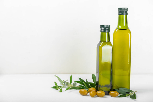 Olivenöl in einer Flasche auf Texturhintergrund. Ölflasche und eine Schale mit Olivenzweigen und -früchten. Platz für Text. Kopierraum. Speiseöl und Salatdressing. - Foto, Bild
