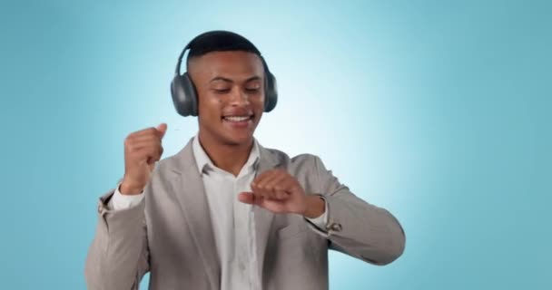 Dancing, headphones and young businessman in studio listening to music, radio or album for fun. Happy, moving and professional male person from Mexico streaming a song or playlist by blue background - Footage, Video