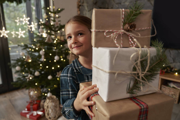 クリスマスプレゼントの山を運ぶ小学生の少女 - 写真・画像