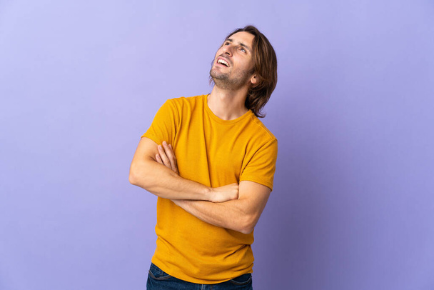 Молодой красивый мужчина изолирован на фиолетовом фоне глядя вверх, улыбаясь - Фото, изображение
