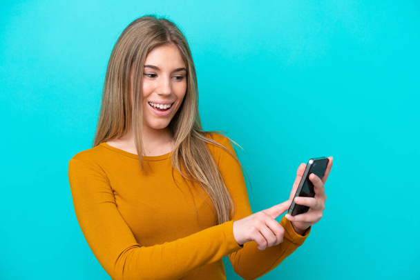 青い背景に隔離された若い白人女性携帯電話でメッセージや電子メールを送る - 写真・画像