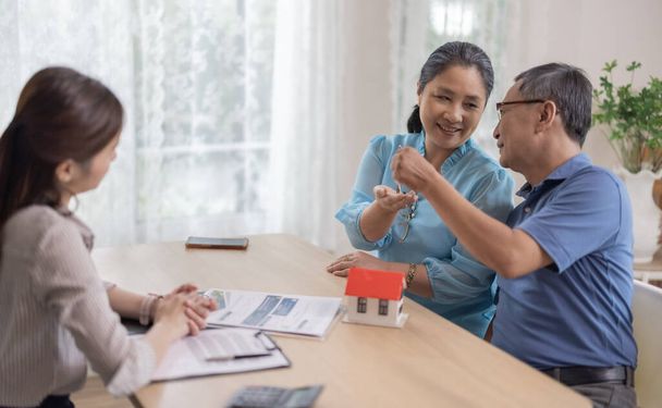 Elderly couples satisfying service in purchasing retirement residence. A detailed contract with saleswoman ensures a smooth transition, including key handovers after agreement on terms and conditions - Photo, image