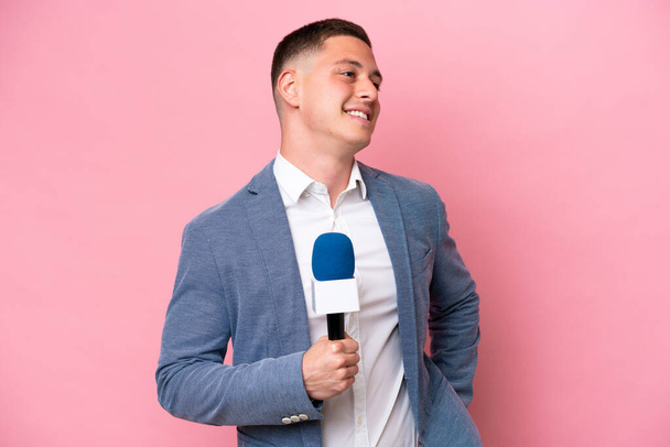 Fiatal brazil műsorvezető férfi elszigetelt rózsaszín háttér pózol karokkal csípő és mosolygós - Fotó, kép