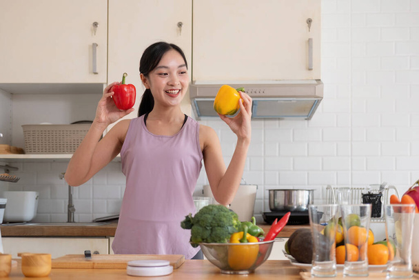 Joven asiática sana hermosa mujer con ropa casual es sonrisa y cortar fruta fresca a dieta en casa en la cocina en vacaciones. - Foto, imagen