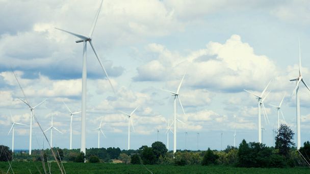 Postępowy sposób wykorzystania wiatru jako odnawialnego źródła energii do zasilania nowoczesnego stylu życia przez farmę turbin wiatrowych na zielonym polu lub wzgórzu. Generator wiatraków wytwarza energię elektryczną bez emisji CO2. - Zdjęcie, obraz