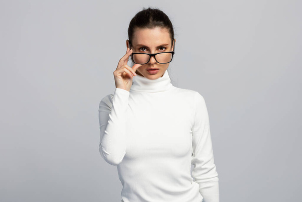 Retrato de una mujer atractiva con gafas, top blanco, estilo de negocios, sobre fondo gris claro - Foto, imagen