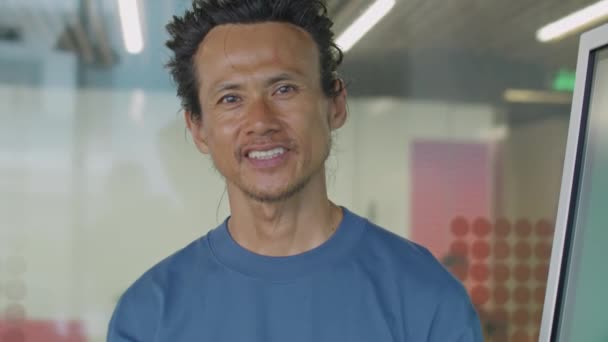 Muotokuva iloinen keski-ikäinen aasialainen mies katselee kameraa ja hymyilee seistessään kokoushuoneessa vieressä digitaalisen näytön toimistossa - Materiaali, video