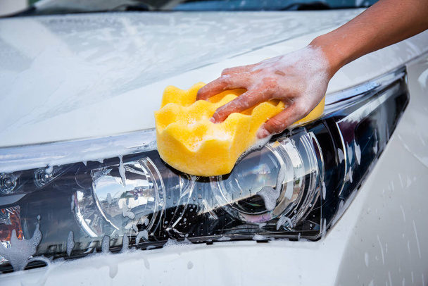 Mano donna con spugna gialla lavaggio fari auto moderna o pulizia auto. concetto di autolavaggio - Foto, immagini