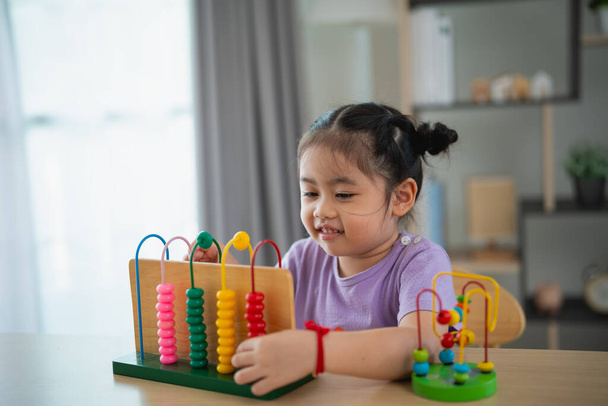 Nuori söpö aasialainen vauva tyttö oppii helmitaulu värillisiä helmiä oppia luottamaan pöydälle olohuoneessa kotona. Lapsi vauva tyttö kehittäminen opiskelu käsite. - Valokuva, kuva