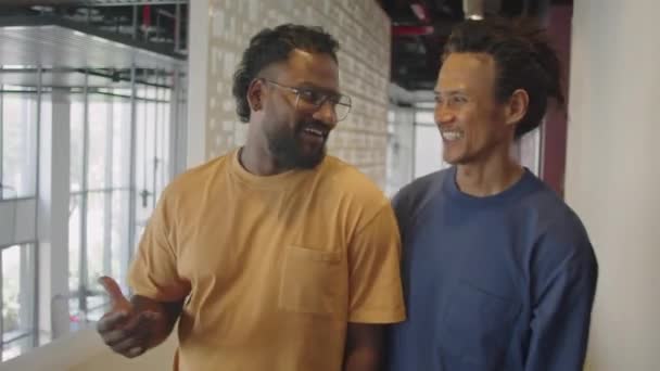 Plan moyen de collègues masculins multiethniques marchant dans le couloir du bureau, souriant et bavardant - Séquence, vidéo