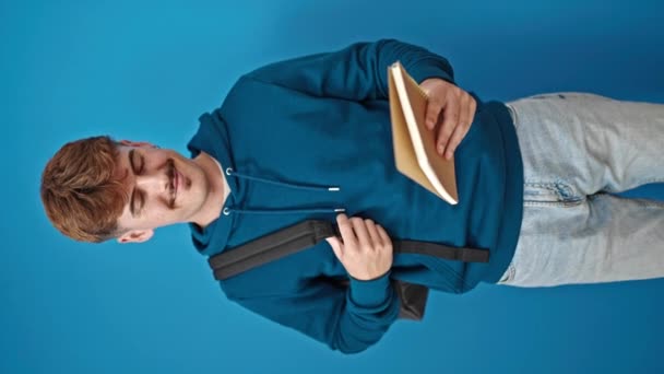 Giovane ispanico uomo studente lettura libro che celebra su isolato sfondo blu - Filmati, video