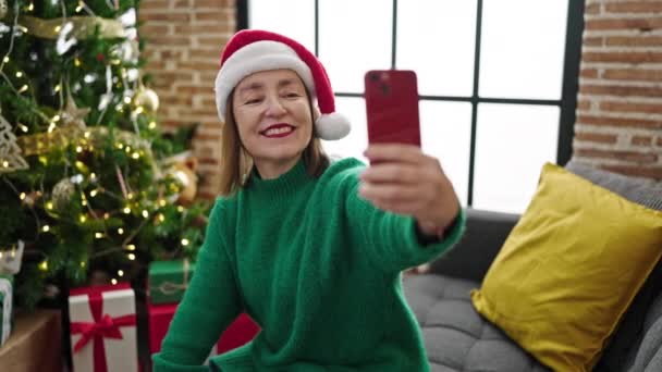 Mujer hispana madura con el pelo gris tomando una foto selfie sentada en el sofá en casa - Metraje, vídeo