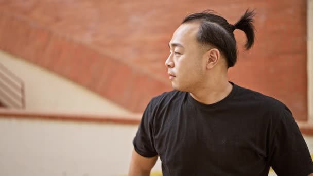 Hombre chino guapo, irradiando confianza, sonriendo alegremente y mostrando su peinado de coleta mientras disfruta del aire libre, alegremente de pie en una vibrante calle de la ciudad con los brazos relajados cruzados. - Imágenes, Vídeo