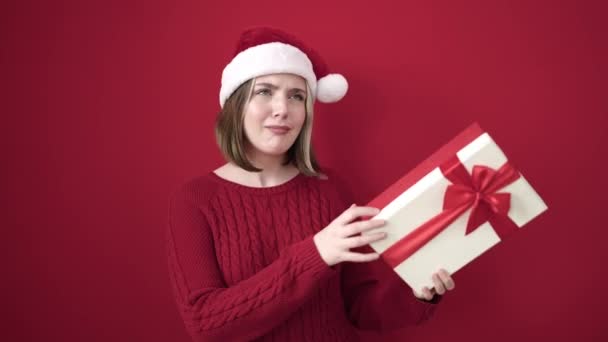 Jonge blonde vrouw met kerst hoed horen gift geluid over geïsoleerde rode achtergrond - Video