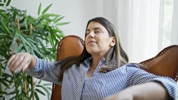 Junge schöne hispanische Frau sitzt zu Hause auf der Couch und hat die Hände über dem Kopf - Filmmaterial, Video