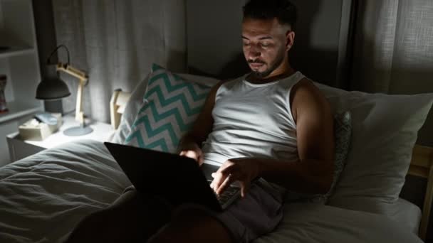 Молодой араб использует ноутбук, сидя на кровати напряжены в спальне - Кадры, видео