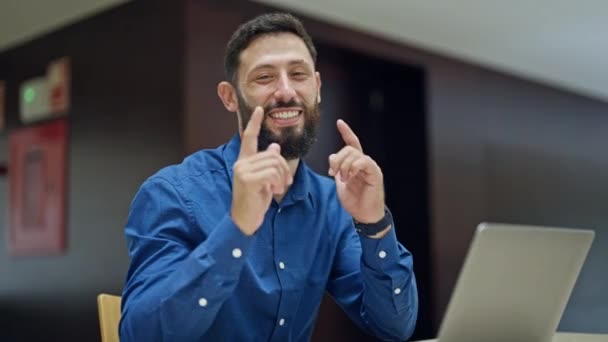Joven trabajador de negocios hispano usando laptop apuntando a cámara haciendo un gesto de pulgares hacia arriba en la oficina - Metraje, vídeo
