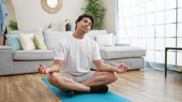 Joven latino sentado en el suelo entrenando yoga estirando la cabeza en casa - Imágenes, Vídeo