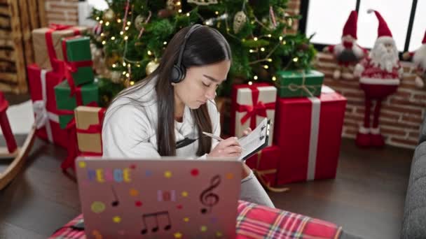 Joven mujer hispana hermosa usando laptop y auriculares escribiendo en el documento en casa - Metraje, vídeo