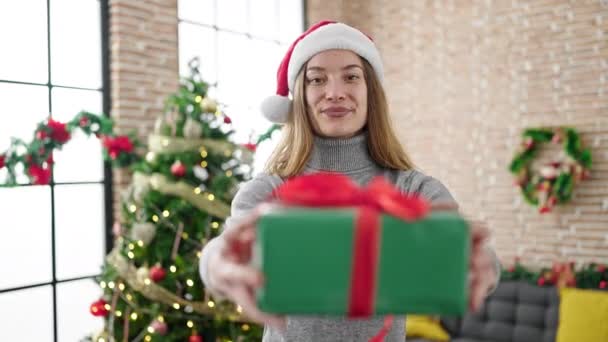 Joven mujer caucásica sosteniendo regalo de Navidad de pie en casa - Metraje, vídeo