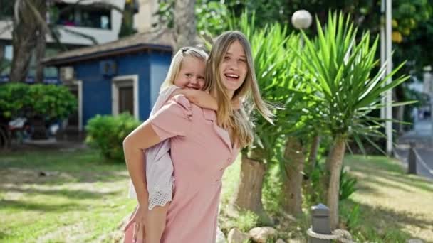 Mère confiante souriant joyeusement tout en se tenant dans un parc verdoyant, tenant sa fille joyeuse sur son dos jouissant de la nature - Séquence, vidéo