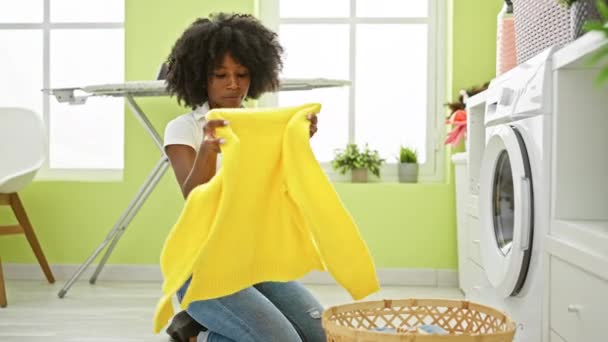 Afrikai amerikai nő mosás ruhák összecsukható pulcsi a mosókonyhában - Felvétel, videó