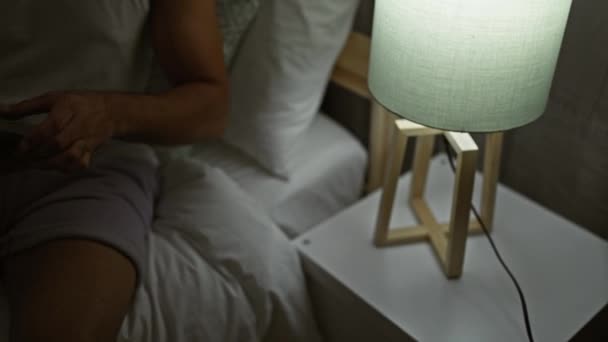 Fiatal arab férfi használ okostelefon ül az ágyban a hálószobában - Felvétel, videó