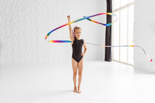 Ritmische gymnastiek. Preteen meisje atleet ritmische gymnastiek in zwart pak doet oefening met kunstlint. Professionele kindersporten. Kopieerruimte - Foto, afbeelding