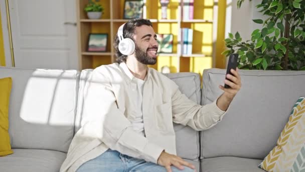 Junger hispanischer Mann mit Videoanruf sitzt zu Hause auf Sofa - Filmmaterial, Video