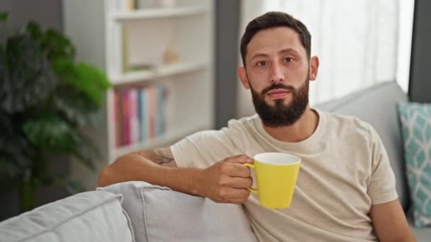 Genç İspanyol adam evdeki kanepede kahve içiyor. - Video, Çekim