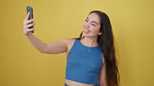 Fiatal gyönyörű spanyol nő mosolygós magabiztos birtoklás videó hívás izolált sárga háttér - Felvétel, videó